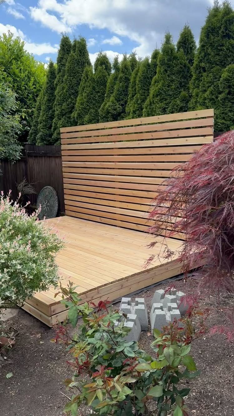 19 Small Backyard Wooden Deck Ideas 10 A wooden deck with a tall horizontal slat privacy screen in a lush backyard garden.
