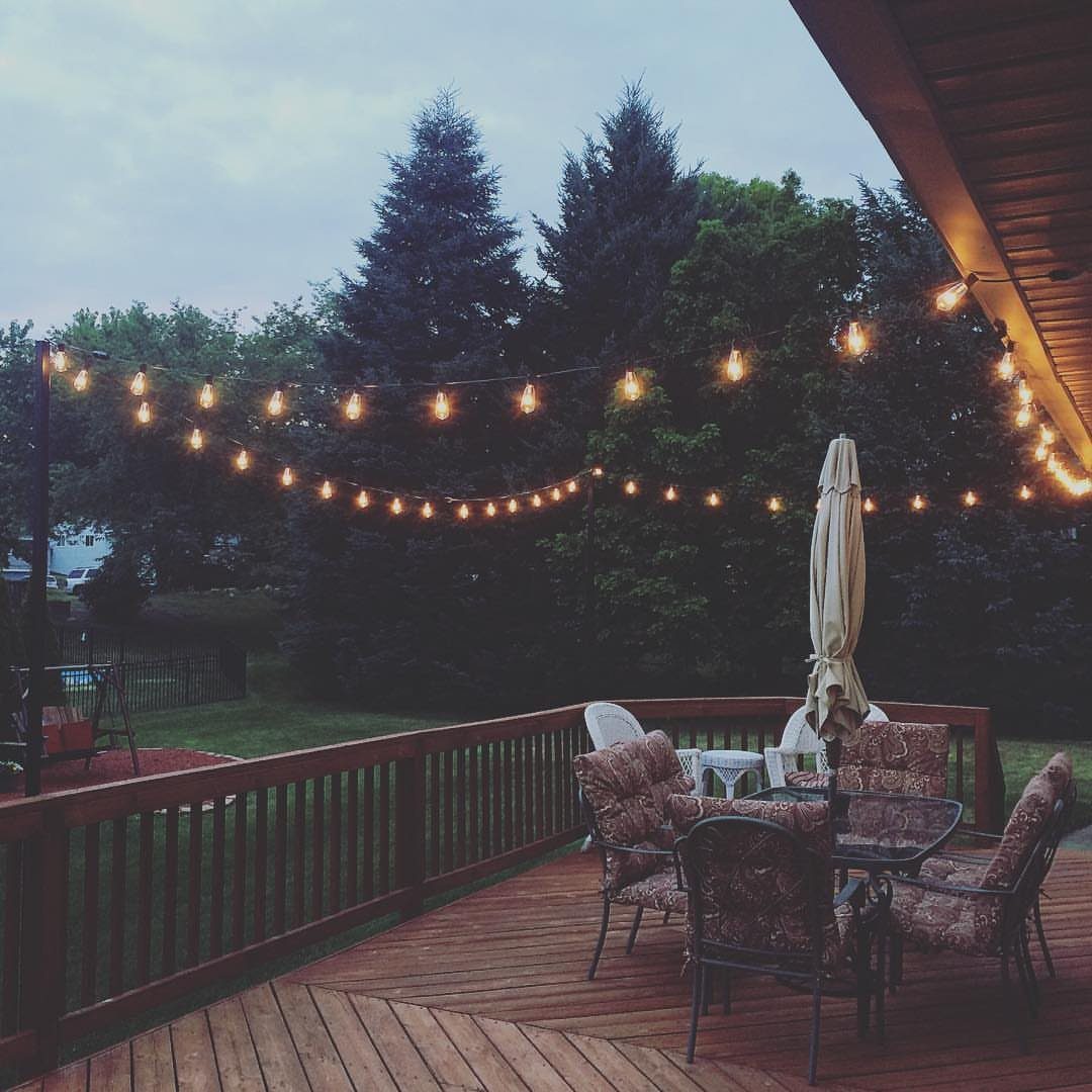19 Small Backyard Wooden Deck Ideas 12 String lights glow over a wooden deck with patio furniture and trees in the background.