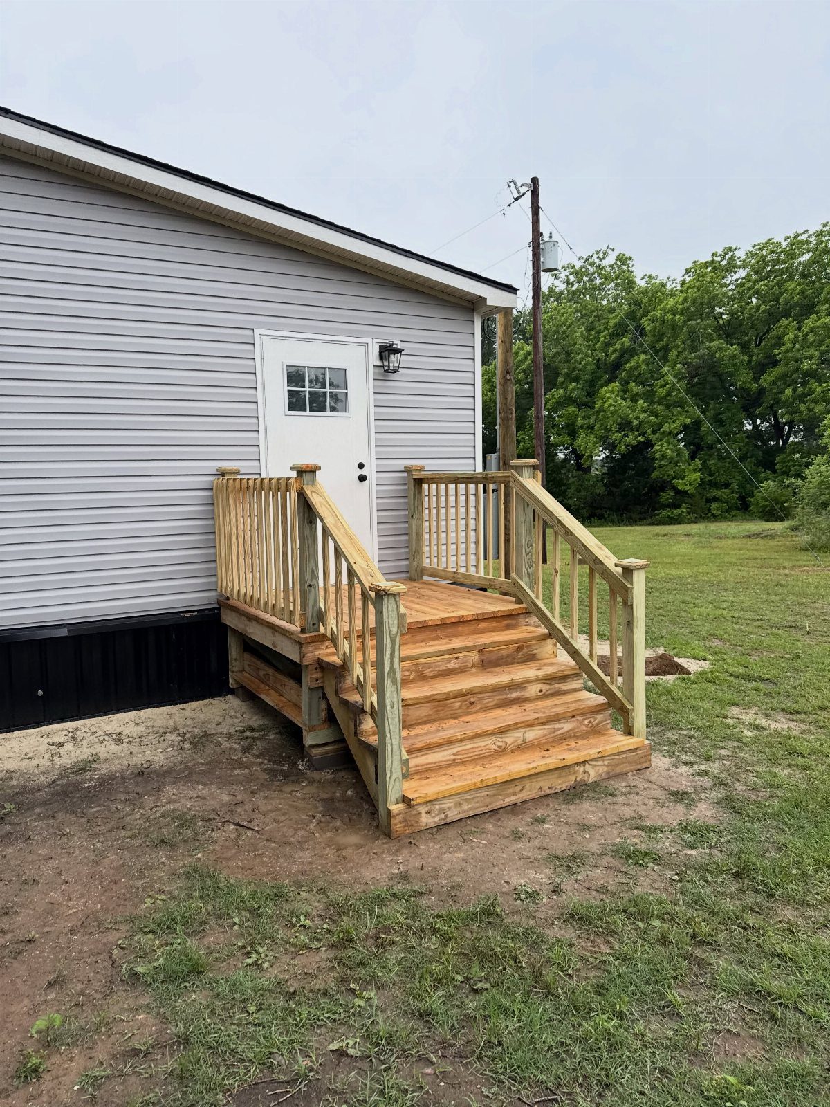 19 Small Backyard Wooden Deck Ideas 16 Small wooden deck with stairs and railings attached to a grey house with a white door.