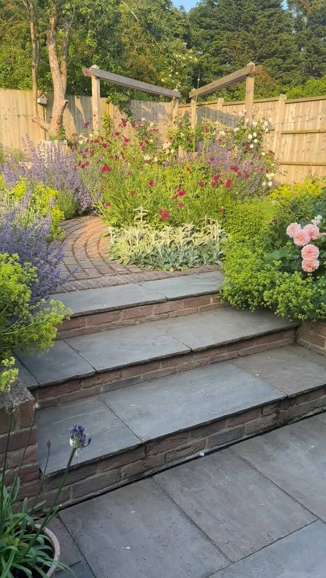19 Small Garden Design Ideas with Built-In Planning Tips 12 Layered garden plants with varying heights surround stone steps and a brick path.