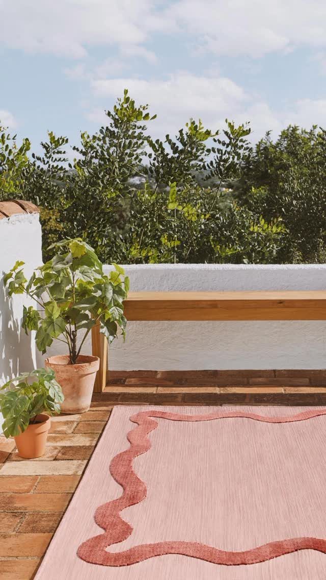 19 Small Garden Design Ideas with Built-In Planning Tips 5 Pink outdoor rug with wavy borders on a terracotta tiled patio next to potted plants.