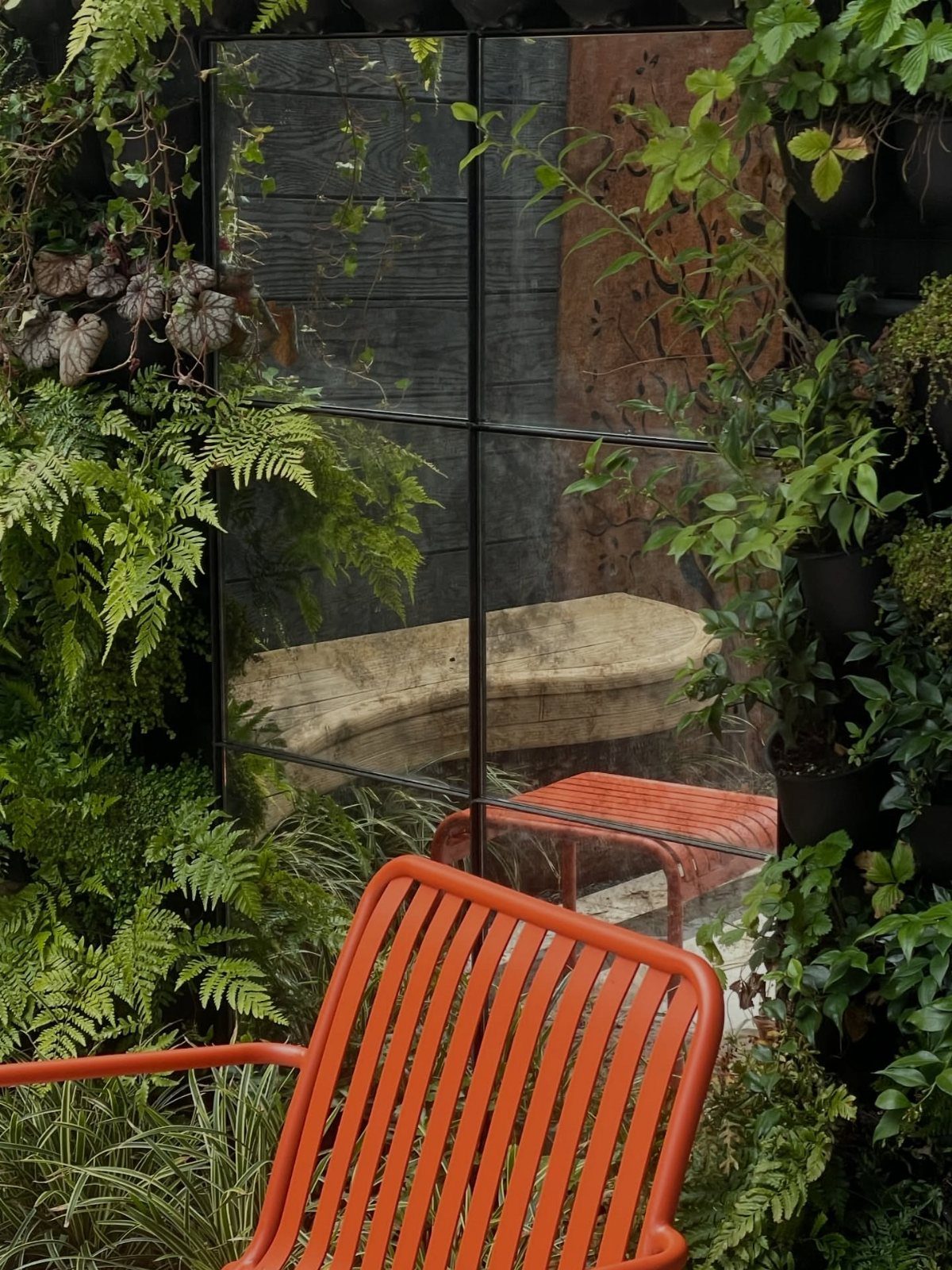 19 Small Garden Design Ideas with Built-In Planning Tips 3 Large black-framed mirror reflecting a stone bench and lush green plants in a small garden.