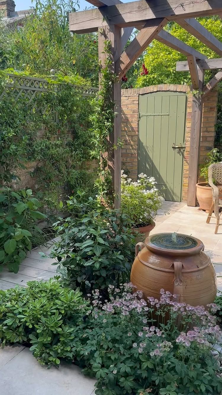 19 Small Garden Design Ideas with Built-In Planning Tips 8 Terracotta jar water feature bubbling amidst green plants and pink flowers in a garden.