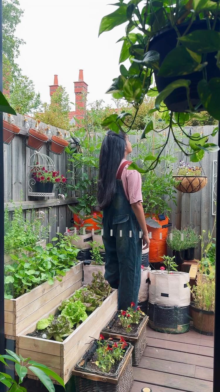 12 Tiny Garden Ideas for Patios, Balconies and Small Yards 2 A person standing amidst various potted plants and wooden planter boxes on a small wooden deck.