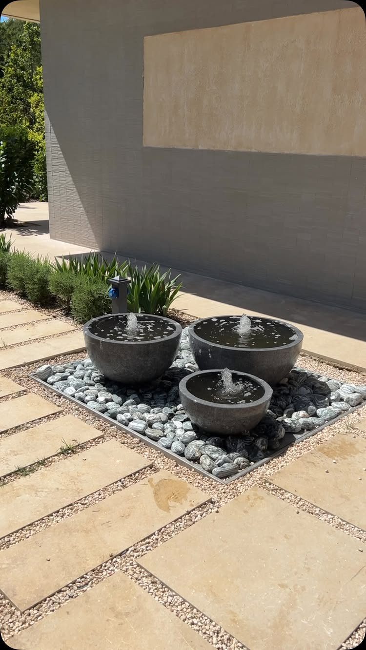 12 Tiny Garden Ideas for Patios, Balconies and Small Yards 8 Three stone water fountain bowls resting in a bed of grey river rocks on a patio.
