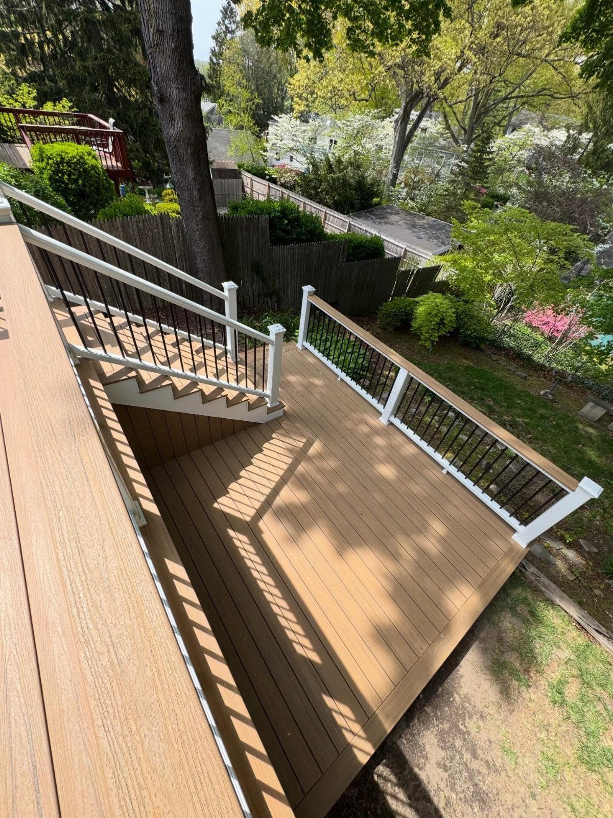 12 Trex Deck Floor Designs for Picture Frames to Herringbone 11 Light brown composite deck with white railings and black spindles overlooking a lush green garden.