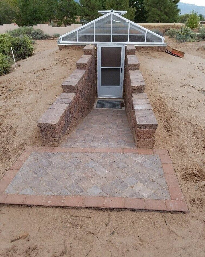 Under Ground Greenhouse: 5 Ways to Grow Below the Surface 5 An underground greenhouse with a glass roof and brick walkway in a sandy landscape.