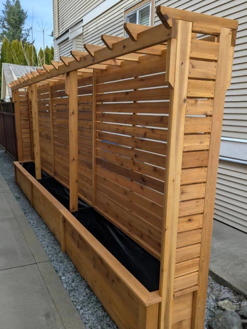 Wood Planter Box: 11 Ideas from Scrap Builds to Built-In Benches 2 A long wooden planter box with a tall horizontal slat trellis and pergola top structure.