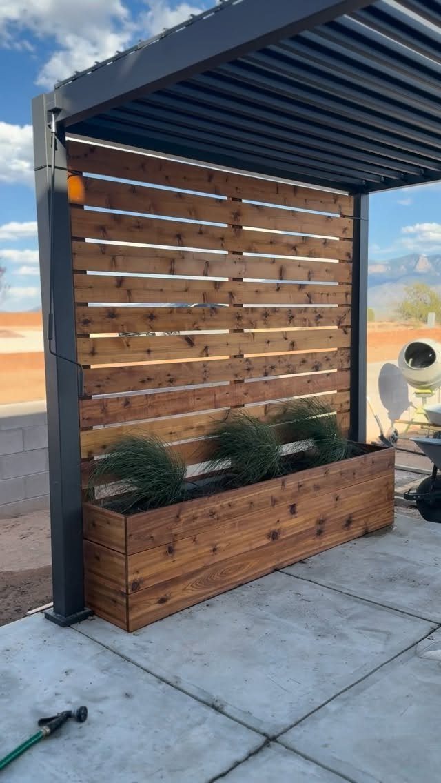 Wood Planter Box: 11 Ideas from Scrap Builds to Built-In Benches 5 A long wooden planter box positioned in front of a horizontal wooden slat privacy screen.