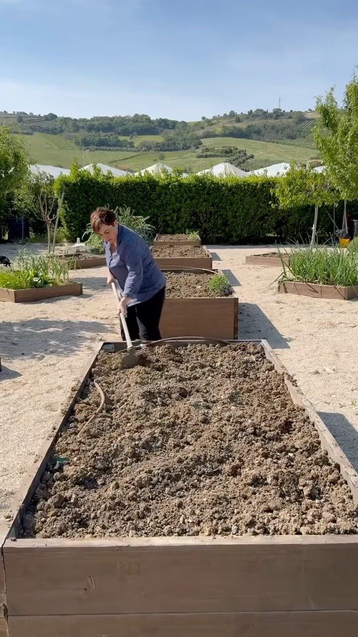 Wood Planter Box: 11 Ideas from Scrap Builds to Built-In Benches 10 A person shoveling soil into a large rectangular wooden raised garden bed outdoors.