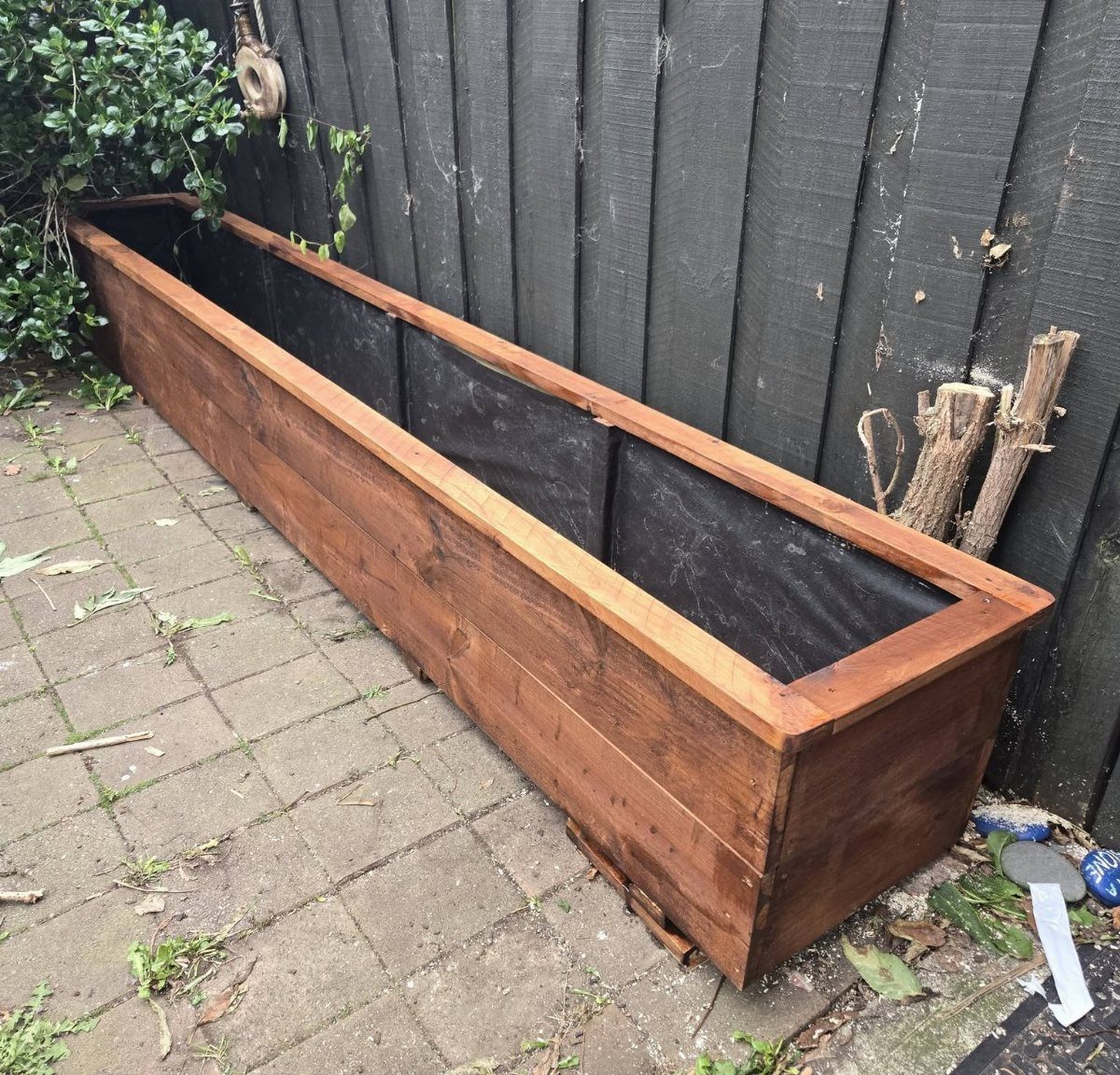 Wood Planter Box: 11 Ideas from Scrap Builds to Built-In Benches 11 A long rectangular wooden planter box lined with black fabric sitting on a stone patio.
