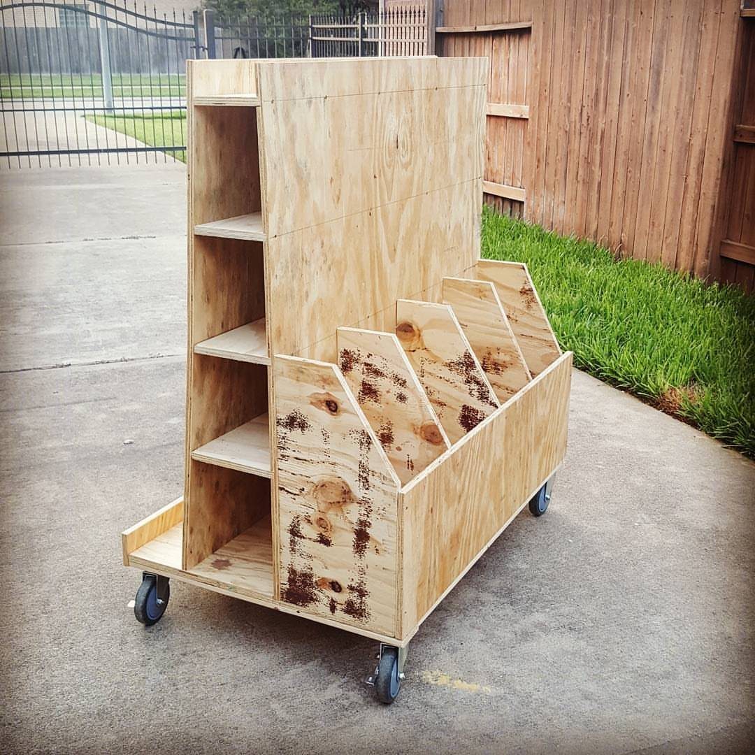 A wooden rolling storage cart with slanted bins and open shelves on wheels.
