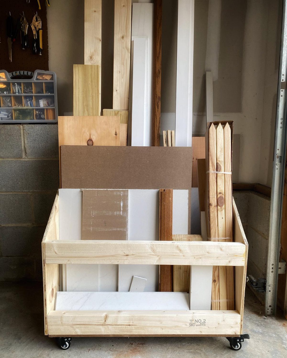 A wooden rolling scrap bin filled with various pieces of lumber and wood scraps in a garage.