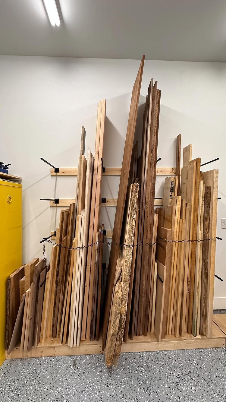 Vertical wood planks stored in a wooden rack with metal pegs against a white wall.